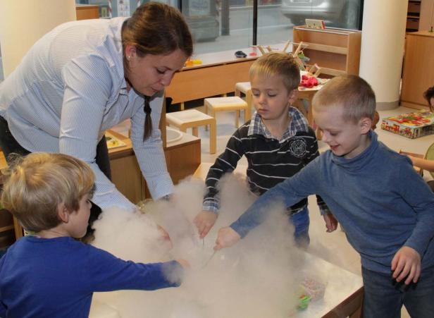 Eine Frau und drei Kinder experimentieren mit Trockeneis in einem Raum.