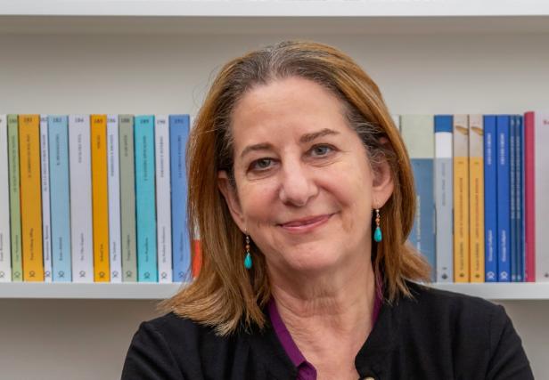 Frau mit schulterlangem Haar vor einem Regal mit bunten Büchern.