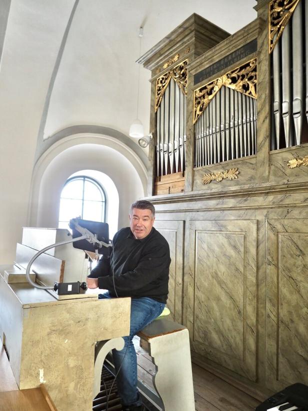 Ein Mann sitzt an einer verzierten Kirchenorgel mit silbernen Pfeifen und goldenen Akzenten.