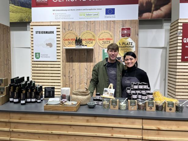 Zwei Personen stehen hinter einem Verkaufsstand mit Kürbiskernprodukten, Ölen und Auszeichnungen aus der Steiermark.