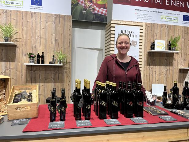 Eine Frau steht hinter einem Verkaufstresen mit mehreren Flaschen Öl oder Essig, Preisschildern und Geschenkboxen.