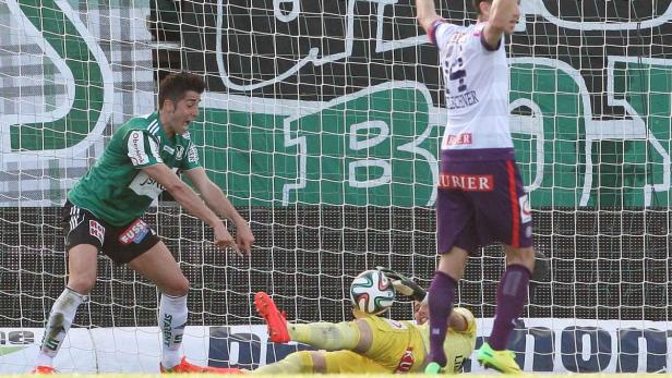 Ein Fußballspieler jubelt, während der Torwart den Ball abwehrt.