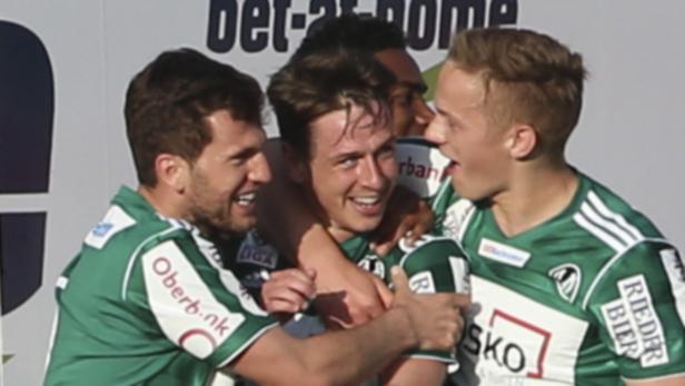 Mehrere Fußballspieler in grünen Trikots umarmen sich und feiern.