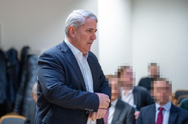Ernst Nevrivy mit grauem Haar und Anzug steht vor einer Gruppe von Personen.