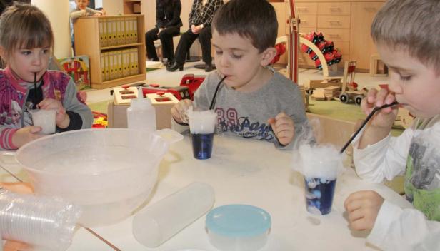 Kinder experimentieren mit Trockeneis und farbigen Flüssigkeiten.