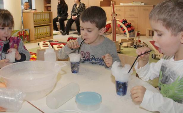 Kinder experimentieren mit Trockeneis und Strohhalmen an einem Tisch.