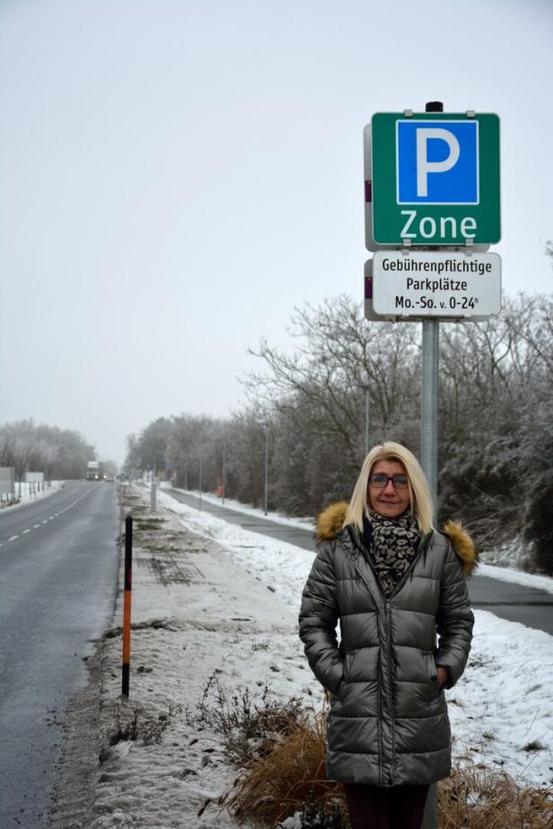 Eine Frau steht neben einem Parkplatzschild in einer winterlichen Landschaft.