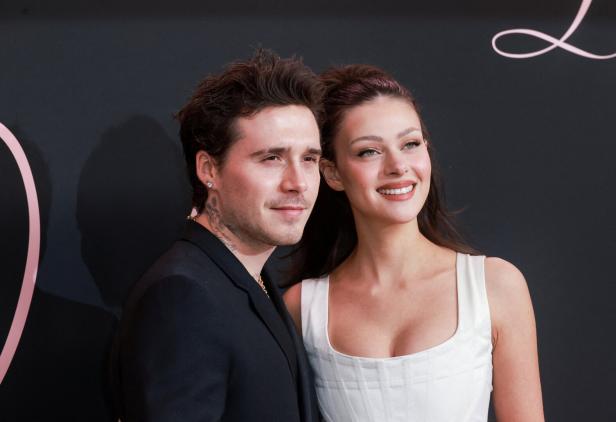 Brooklyn Peltz Beckham und Nicola Peltz Beckham lächeln vor einem dunklen Hintergrund.