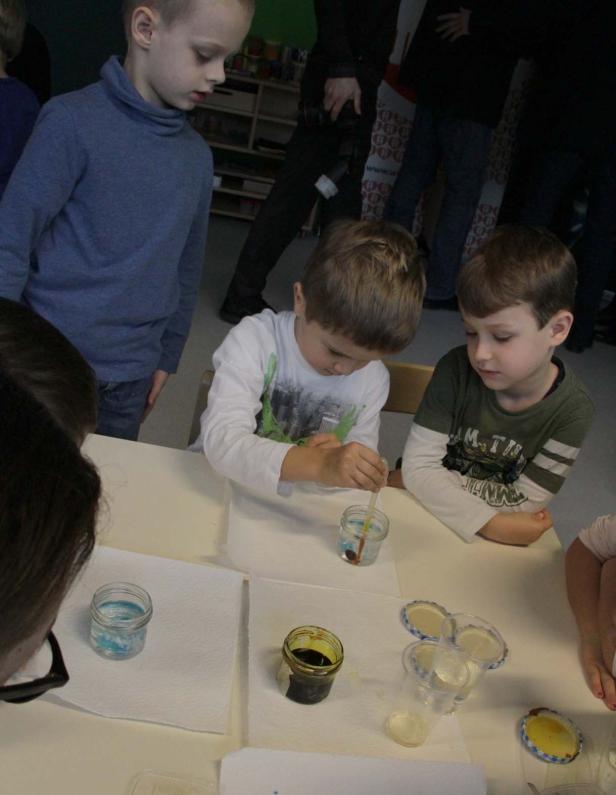 Kinder experimentieren mit Pipetten und farbigem Wasser an einem Tisch.