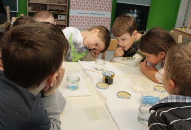 Eine Gruppe Kinder sitzt an einem Tisch und bastelt mit kleinen Gläsern und farbigem Sand.