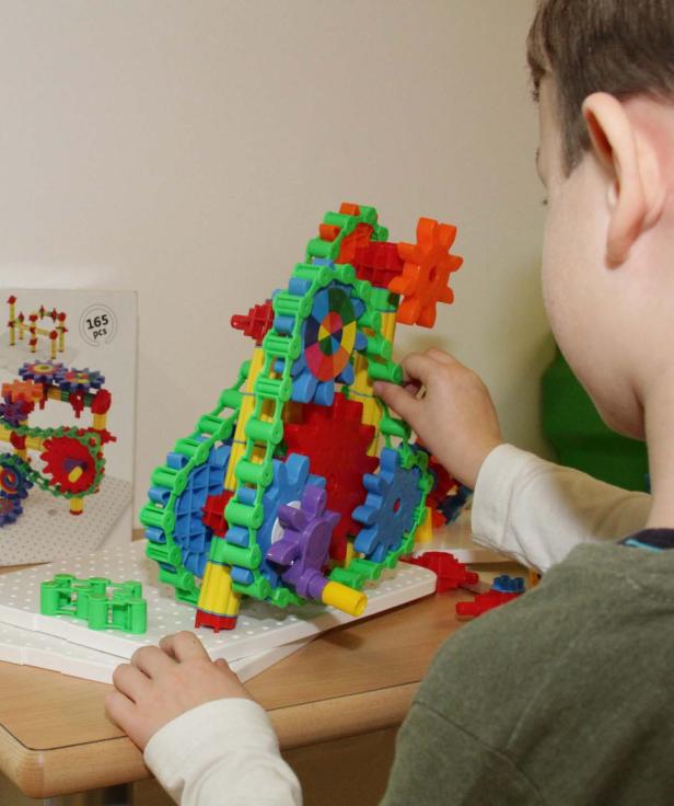 Ein Kind spielt mit einem bunten Konstruktionsspielzeug mit Zahnrädern.