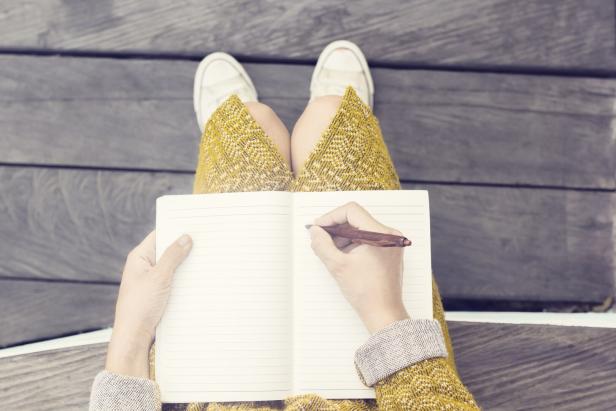 Girl with blank diary and pen sitting on wooden bench