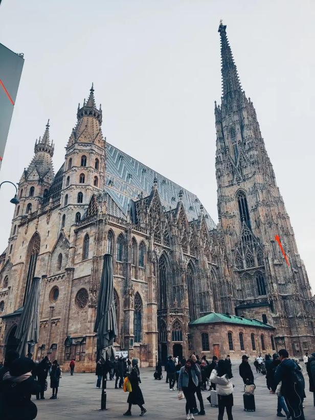 Stephansdom mit Südturm und vielen Menschen auf dem Platz davor bei bewölktem Himmel.