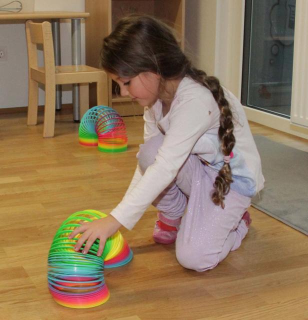Ein Mädchen spielt mit einer bunten Regenbogenfeder auf dem Boden.