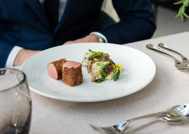 Fein angerichtetes Fleischgericht mit Gemüse und Reis auf weißem Teller in elegantem Ambiente.