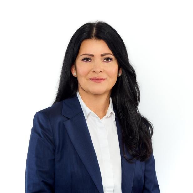 Frau mit langen dunklen Haaren im blauen Blazer vor weißem Hintergrund.