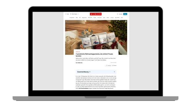 Laptop mit geöffneter Webseite des KURIER, die einen Artikel mit Bild von Händen zeigt, die ein Fotobuch halten, im Hintergrund ein Weihnachtsbaum und eine Decke.