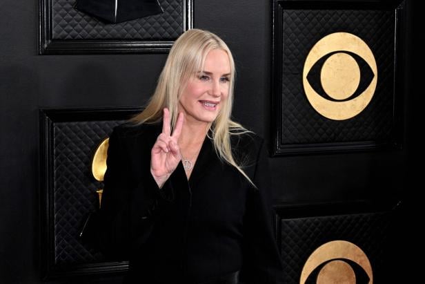 Eine Frau mit langen blonden Haaren trägt Schwarz und zeigt ein Peace-Zeichen mit der Hand.