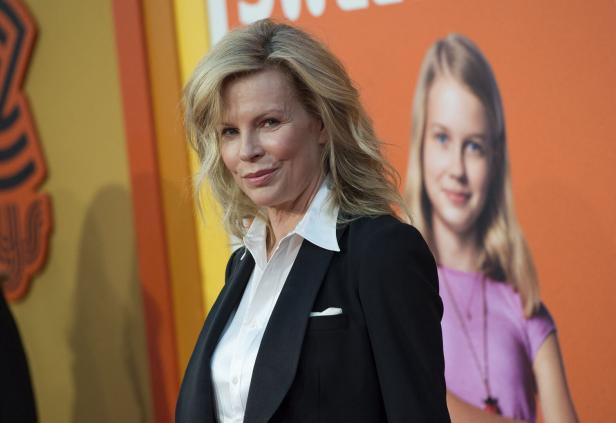 Kim Basinger posiert vor einem orangefarbenen Hintergrund mit einem Mädchenporträt.