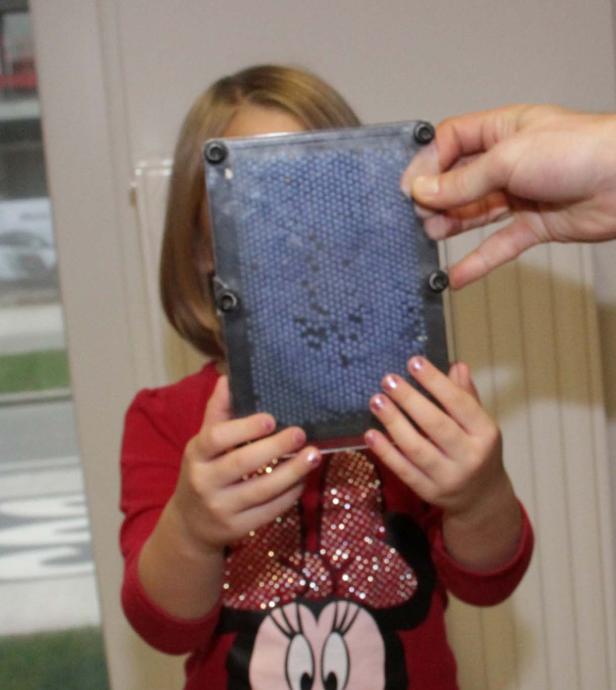 Ein Kind hält ein Nagelbrett vor sein Gesicht, während eine Hand es berührt.