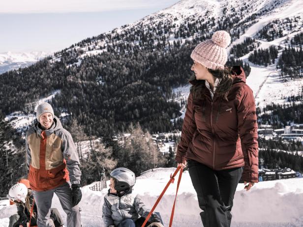 Familie genießt gemeinsam einen Wintertag im Schnee vor verschneiter Bergkulisse am Katschberg.