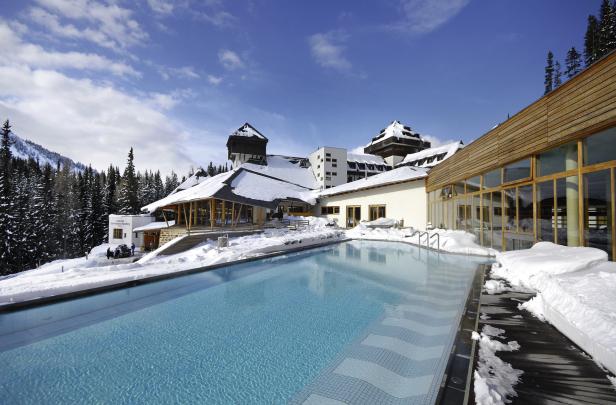 Beheizter Außenpool vor verschneitem Hotelgebäude in winterlicher Berglandschaft.