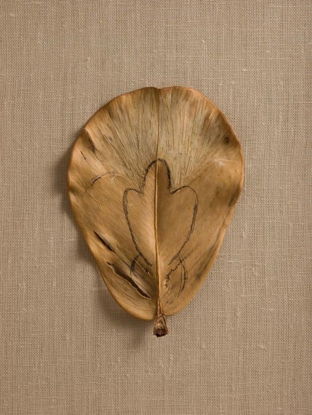 Ein getrocknetes Blatt mit einer Herzzeichnung liegt auf einem beigen Stoff.