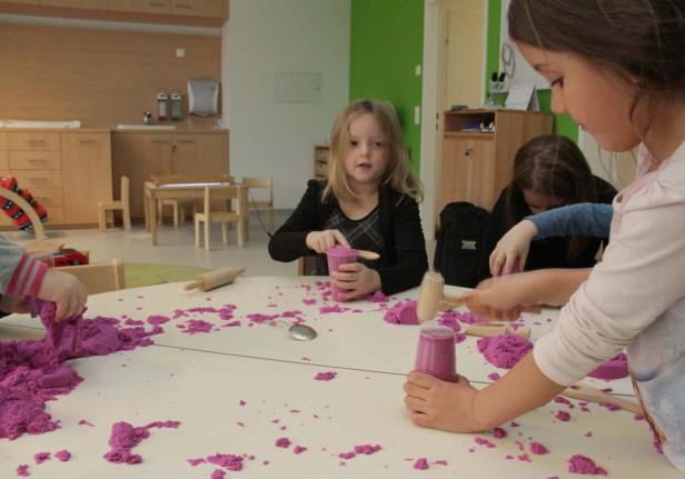 Kinder spielen mit lila Knete an einem Tisch in einem hellen Raum.