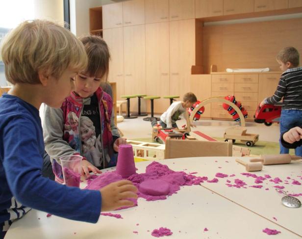 Kinder spielen mit lila Spielsand an einem Tisch in einem Kindergarten.