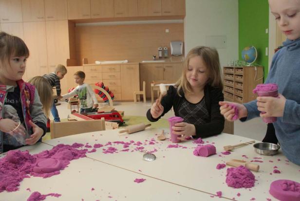 Kinder spielen in einem Kindergarten mit lila Spielsand an einem Tisch.