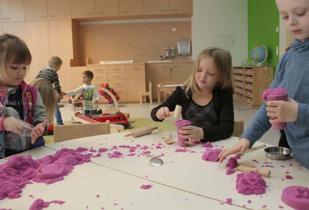 Mehrere Kinder spielen in einem Kindergarten mit lila Spielsand.