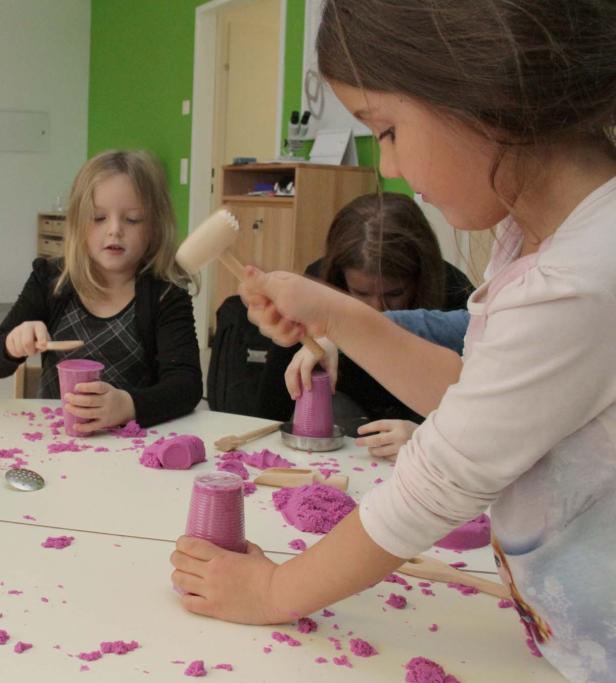 Kinder spielen mit lila kinetischem Sand an einem Tisch.