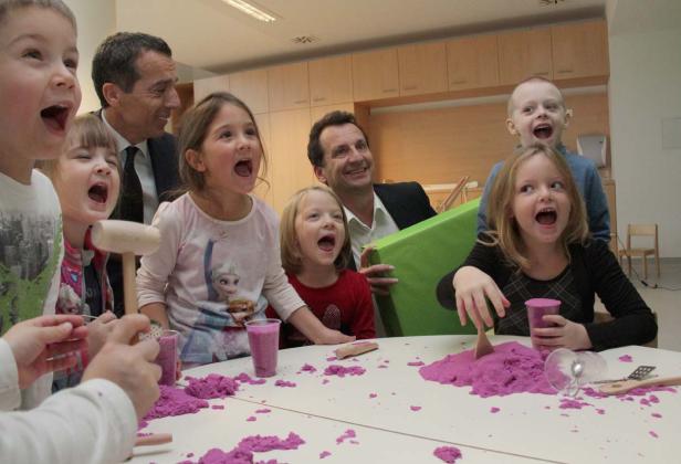 Eine Gruppe aufgeregter Kinder und zwei Männer spielen mit lila Spielsand an einem Tisch.