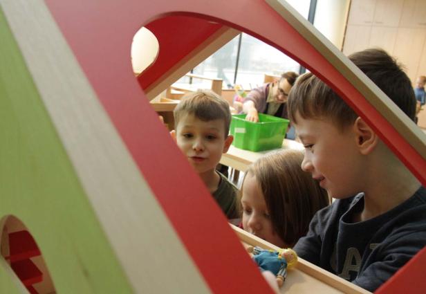 Drei Kinder spielen mit einer Puppe in einem hölzernen Spielhaus.