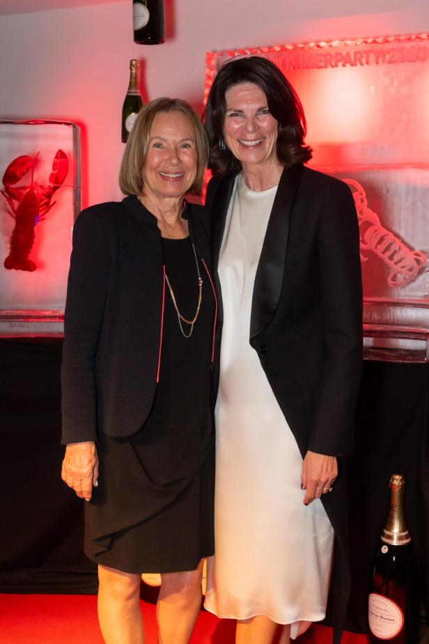 Zwei elegant gekleidete Frauen lächeln vor Hummer- und Champagner-Dekoration.