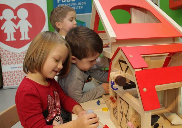 Drei Kinder spielen mit einem hölzernen Bauernhofspielzeug.