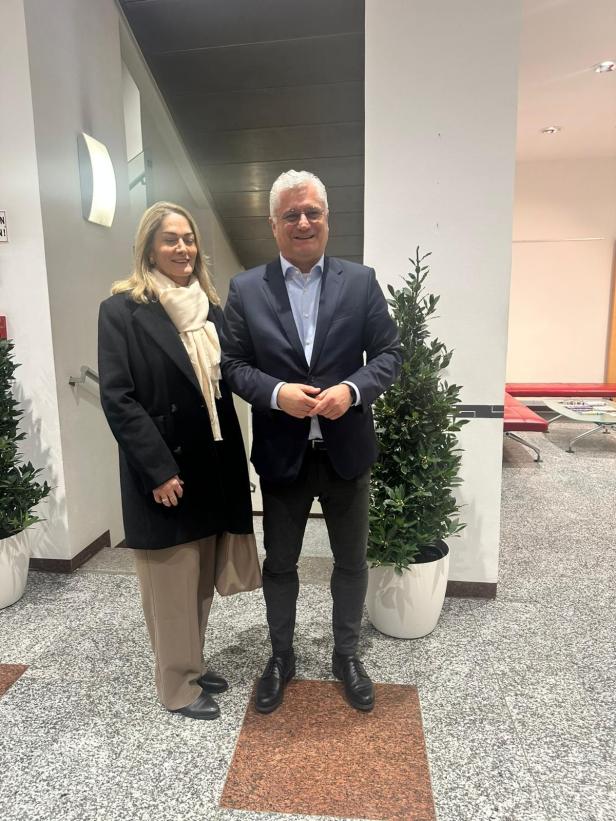 Zwei Personen stehen in einem modernen Innenraum zwischen zwei großen Pflanzen.