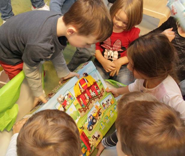Eine Gruppe Kinder betrachtet gespannt ein großes Spielzeugset mit einem Bauernhof.