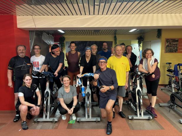 Eine Gruppe von Leuten posiert in einem Fitnessstudio mit Spinning-Rädern für ein Foto.
