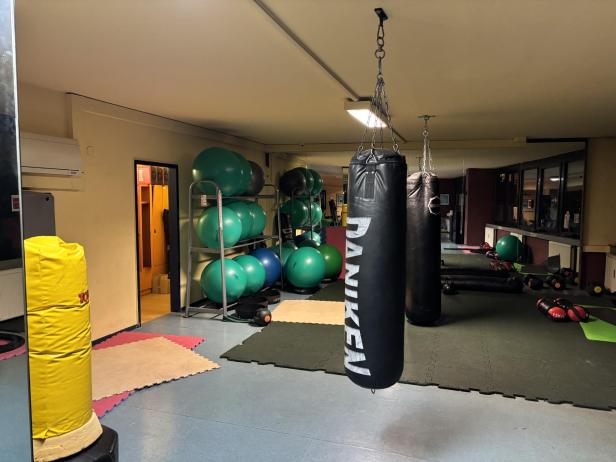 In einem Fitnessstudio hängen Boxsäcke vor einem Spiegel, neben Gymnastikbällen und Trainingsgeräten.