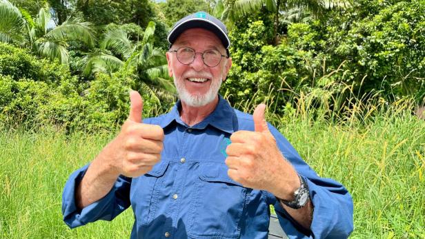 Dr. Bob steht im Dschungel und halt lächelnd die Daumen nach oben.