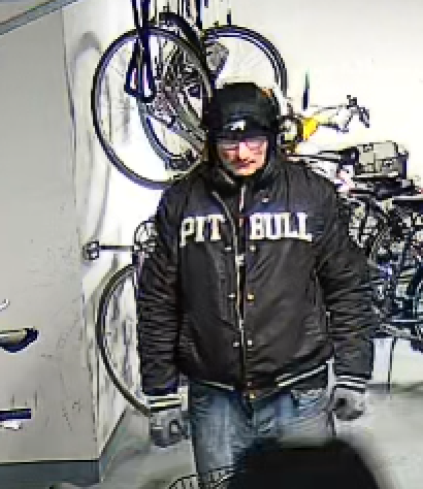 Eine Person mit dunkler Jacke und Mütze steht in einem Raum mit mehreren an der Wand hängenden Fahrrädern.