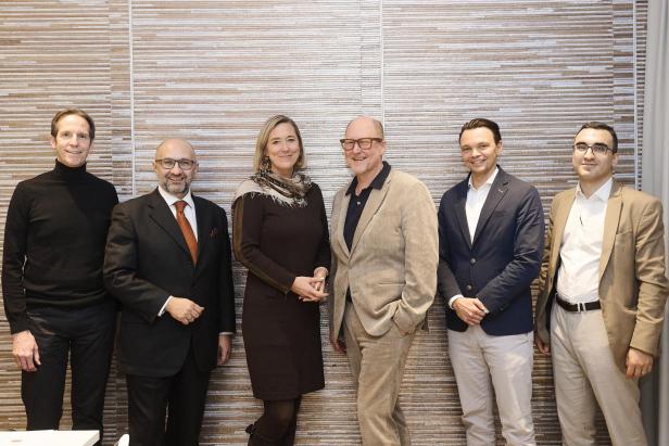 Sechs Ärzt:innen und Expert:innen stehen an einer Wand und lächeln in die Kamera