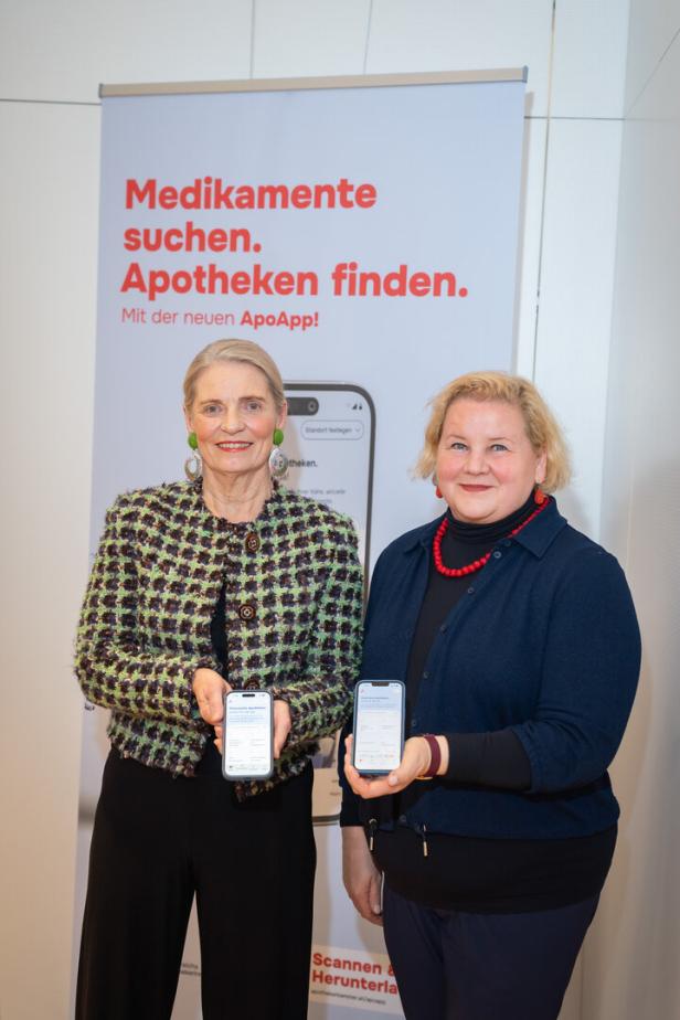 Zwei Frauen stehen vor einem Werbeplakat und halten jeweils ein Smartphone mit geöffneter App in der Hand.