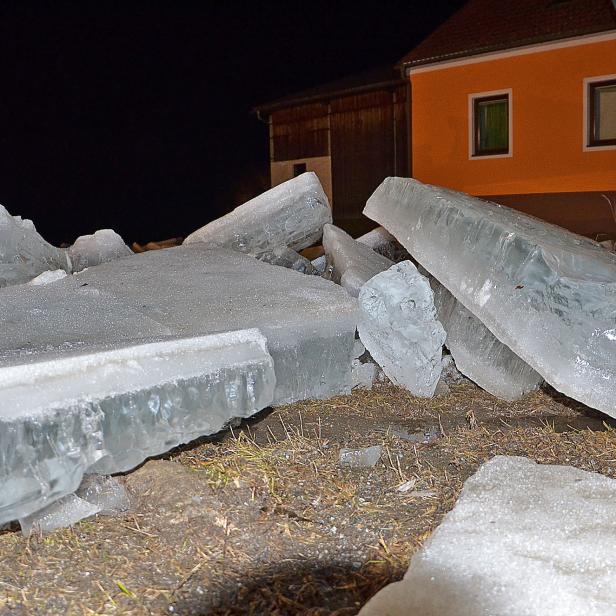 Mehrere Eisschollen liegen am Ufer, im Hintergrund ist ein orangenes Haus zu sehen. Die Aufnahme wurde nachts gemacht.