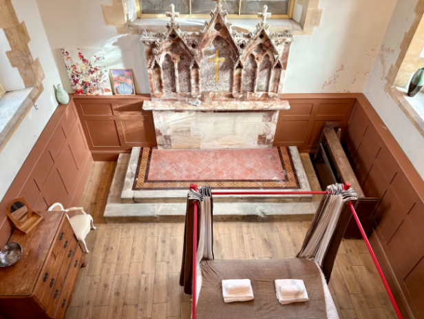 Schlafzimmer mit Himmelbett direkt vor einem historischen Altar in umgebauter Kirche.