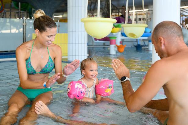 Eine Familie spielt lachend mit einem Kleinkind im Kinderbecken eines Erlebnisbades.