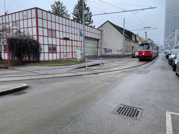 eine rote Straßenbahn fährt an einem Betriebsgelände vorbei