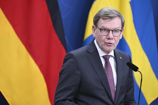 Ein Mann mit Brille spricht vor den Flaggen Deutschlands und Schwedens.