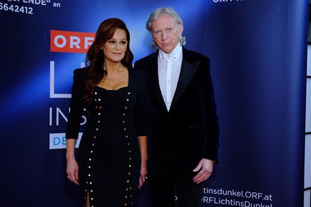 Andrea Berg im eleganten schwarzen Kleid mit goldenen Knöpfen steht neben Uli Ferber im dunklen Anzug vor blauem Hintergrund.